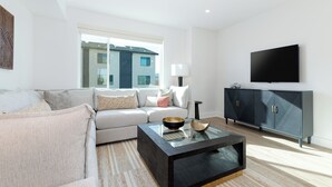 A modern living room with a sofa, coffee table, and a television on the wall. - Charming 3 bed townhome w/direct access to downtown GJ! NO EXTRA FEES! (Grand Junction)