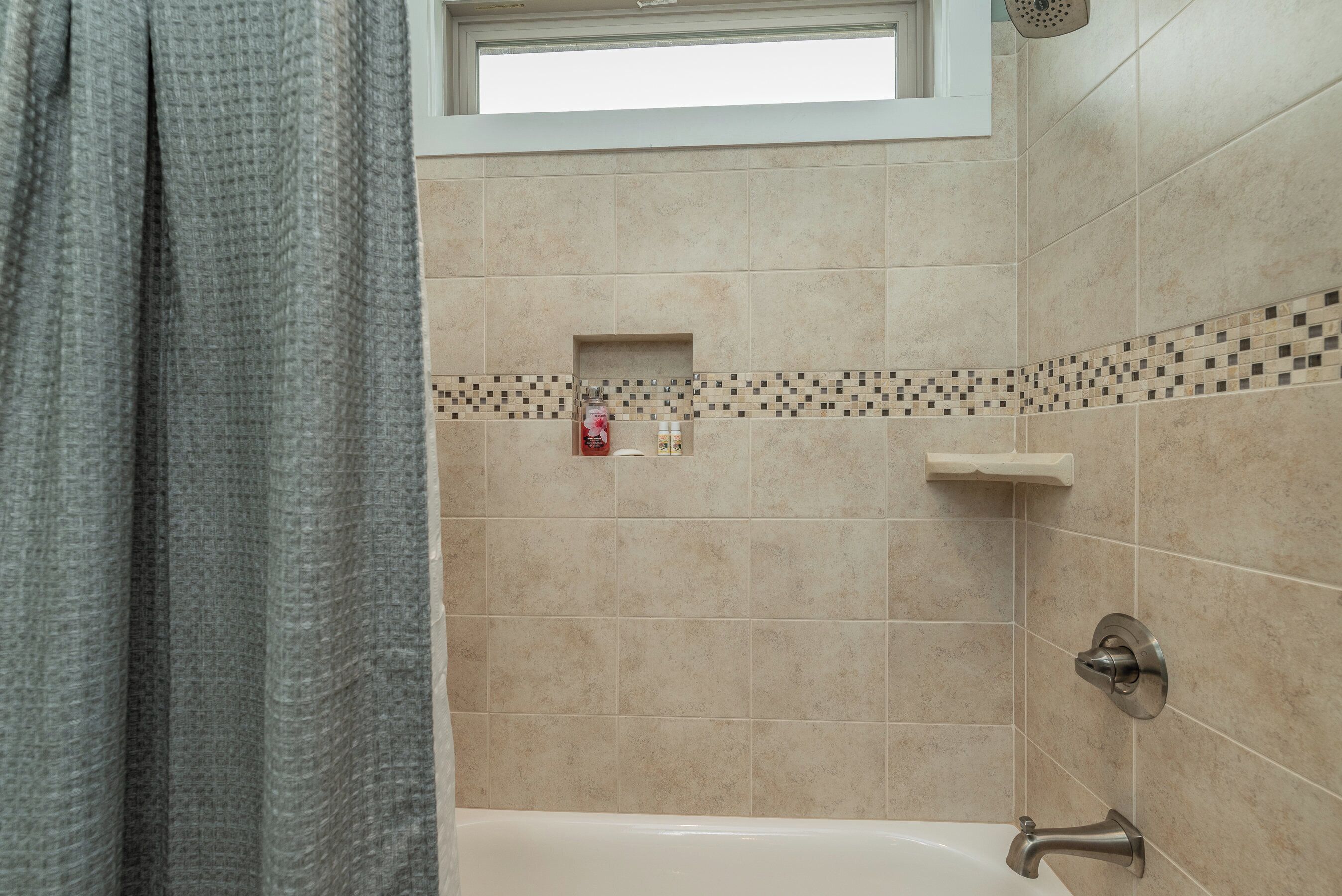 A bathroom with a bathtub, a shower, and a window above the shower.