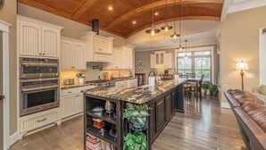A spacious kitchen with a large island, built-in ovens, and a wooden ceiling.