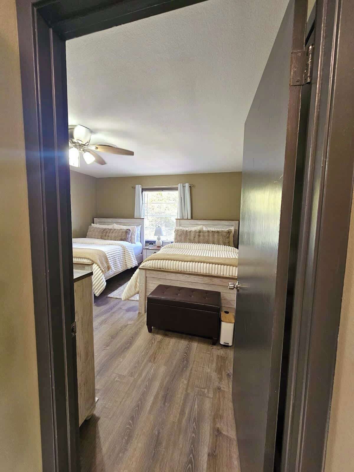 A bedroom with two beds, a ceiling fan, a window with curtains, and a wooden floor.