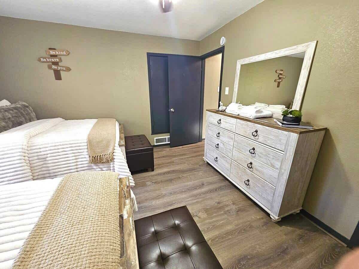 A bedroom with two beds, a dresser, a mirror, and a door.