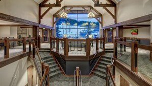 Un intérieur spacieux avec un escalier central, des poutres en bois et une grande fenêtre donnant sur un paysage enneigé.