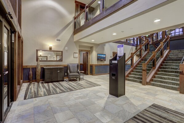 A spacious lobby with a reception desk, a large vase, and a staircase leading to an upper level.