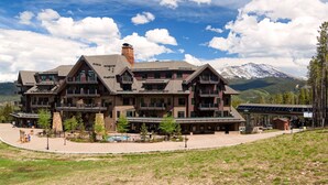 Un grand chalet à plusieurs étages, doté de balcons, d’une piscine et surplombant un paysage montagneux.