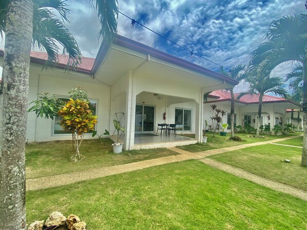 A two-story building with a covered patio area, a lawn, and several potted plants.
