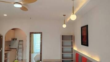 A modern hotel room with a large bed, a ceiling fan, a desk, and a kitchenette.