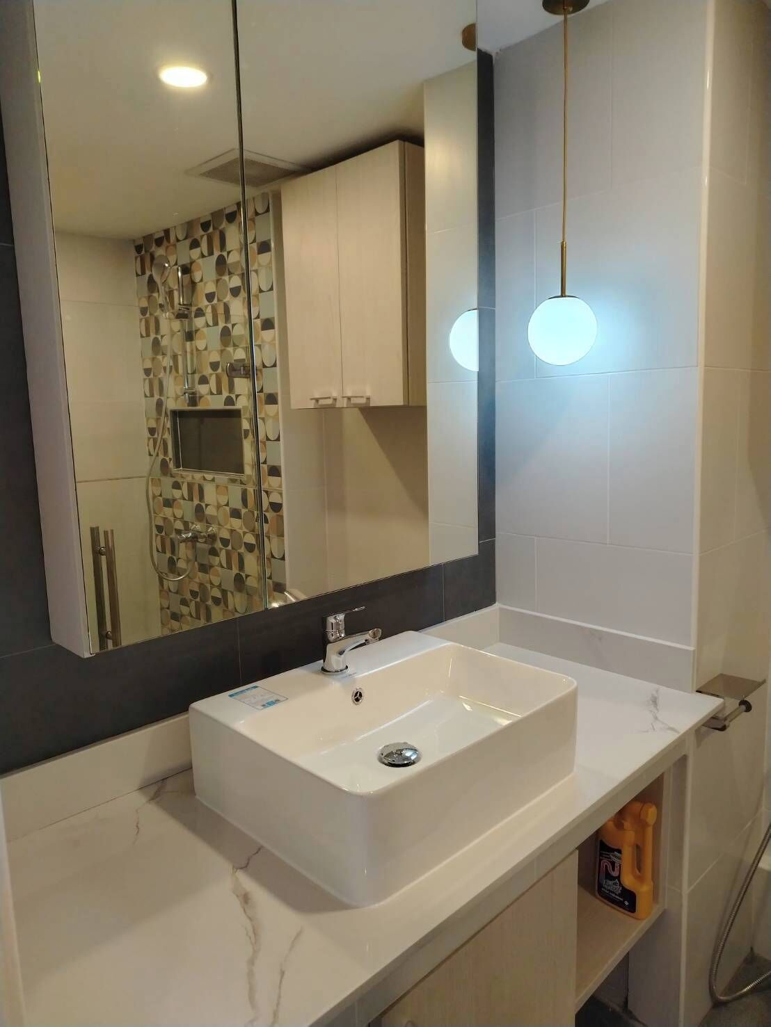 Une salle de bain moderne avec un lavabo rectangulaire blanc, un grand miroir et un luminaire fixé au mur.