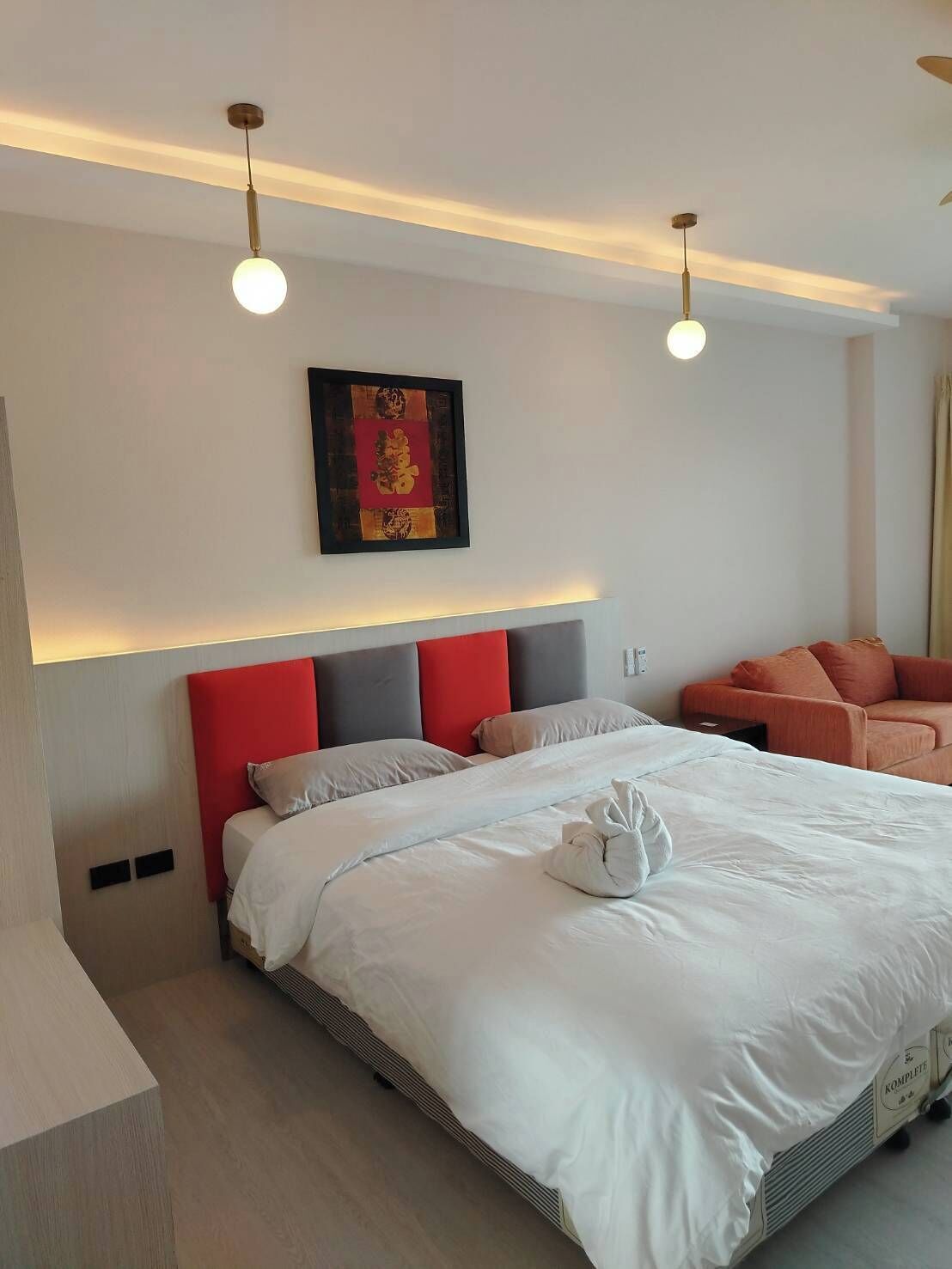 A modern hotel room with a large bed, red and grey headboard, and a single artwork on the wall.