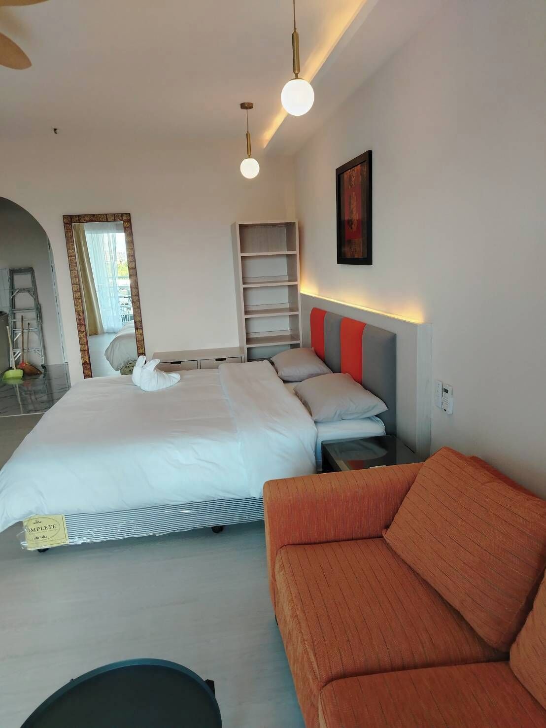 Una habitación de hotel moderna con una cama grande, un sofá, un estante empotrado y un espejo.