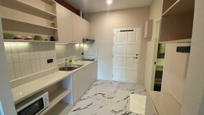 A compact kitchen with white cabinets, a microwave, a sink, and a door leading to another room. - Studio View Talay (Pattaya)