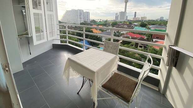 A balcony with a table and chair, a view of a cityscape including a tower, and a building with a red roof. - Studio View Talay (Pattaya)