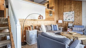 Una sala de estar acogedora con un muro de madera, un sofá, una mesa de centro y una escalera.