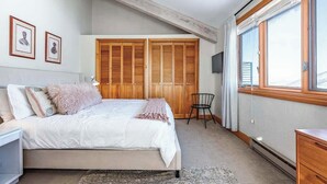 Un dormitorio con cama, armario de madera, una silla, escritorio y ventana.