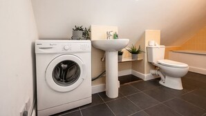 Een kleine badkamer met een voorlader wasmachine, een wastafel op standaard en een toilet.