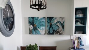 Ein Essbereich mit Holztisch, Stühlen, einer Uhr und zwei floralen Bildern an der Wand.