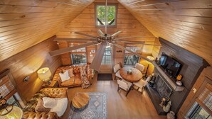 Una habitación acogedora estilo buhardilla con ventilador de techo, chimenea, televisor y un espacio de estar cómodo con sofá y sillones.