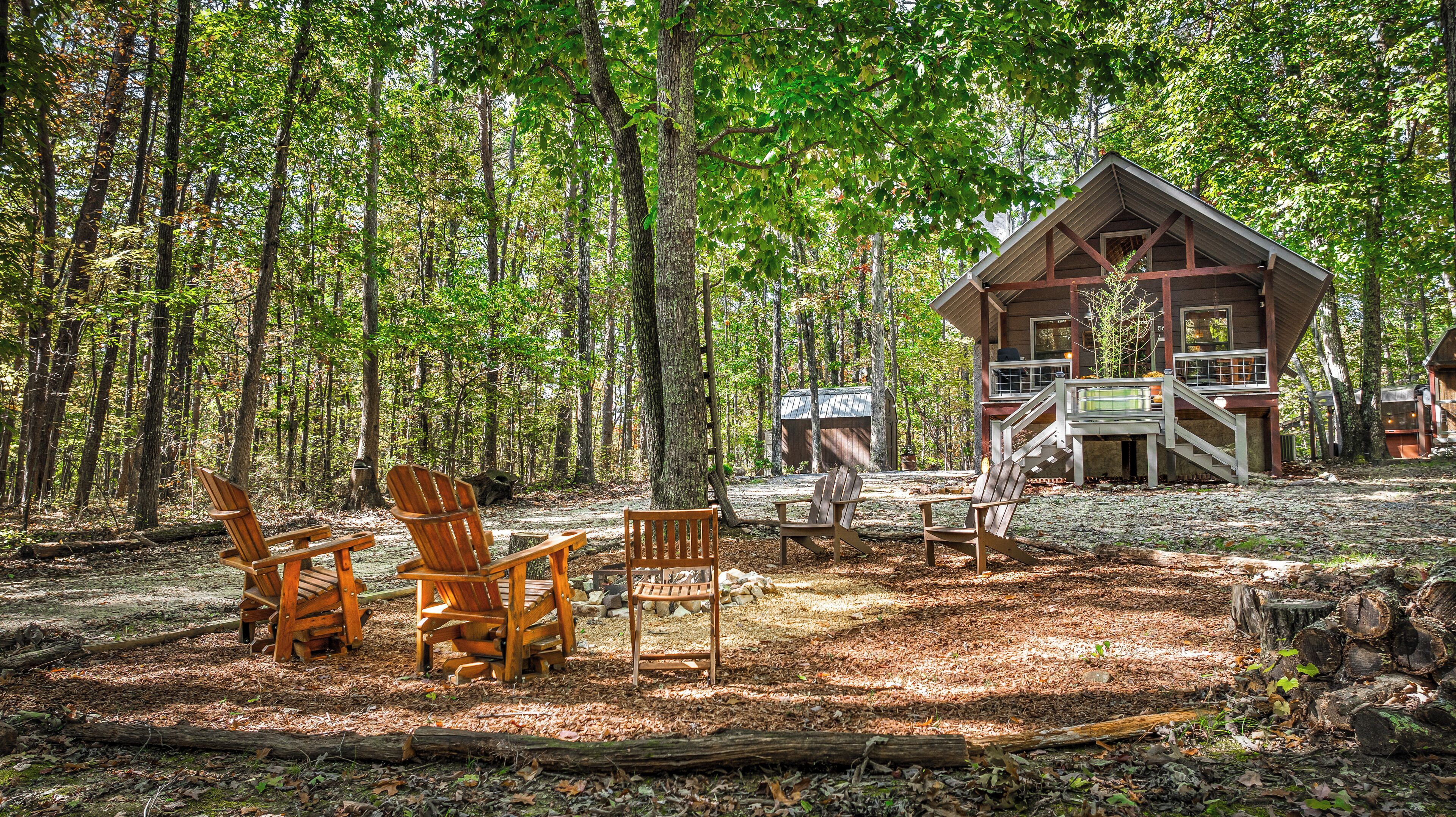 A cabin in a forest with outdoor seating and a deck.