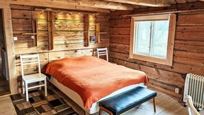 Um quarto de cabana aconchegante, com uma cama, um banco e uma janela.