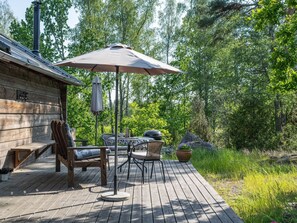 Een houten terras met buitenmeubilair, waaronder een tafel en stoelen, en een grote parasol die schaduw biedt.