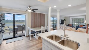 A modern kitchen with a large island, a dining area with a table and chairs, and a living room with a sofa and a TV.