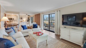 A modern living room with a sofa, coffee table, and a TV. There's a kitchen area with cabinets and a microwave.