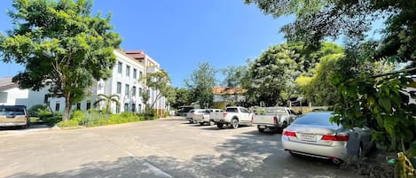 A parking area with several cars and a white building with a red roof.