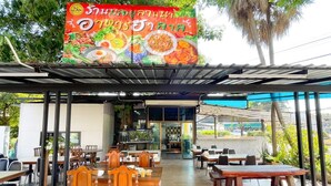 An outdoor dining area with wooden tables and chairs, a covered seating area, and a signboard displaying food items. - Tamnak Lanta at Chiang Mai (Chiang Mai)