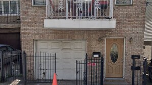 A two-story brick building with a garage door, a gated entrance, and a balcony. - Karan luxury apartment (Jersey City)