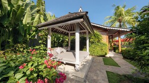 A gazebo with a tiled roof and a bench, surrounded by lush greenery and flowering plants. - Villa Taramille by Villa Finder (Kerobokan)