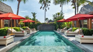 Une piscine entourée de palmiers et de verdure, avec des chaises longues et des parasols rouges.