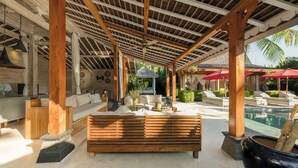 Un espacio al aire libre techado con un banco de madera, sillones de descanso y una piscina.