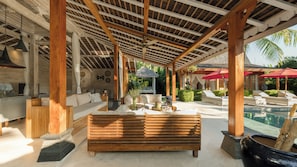 Un espace extérieur abrité comprenant un banc en bois, des fauteuils et une piscine.