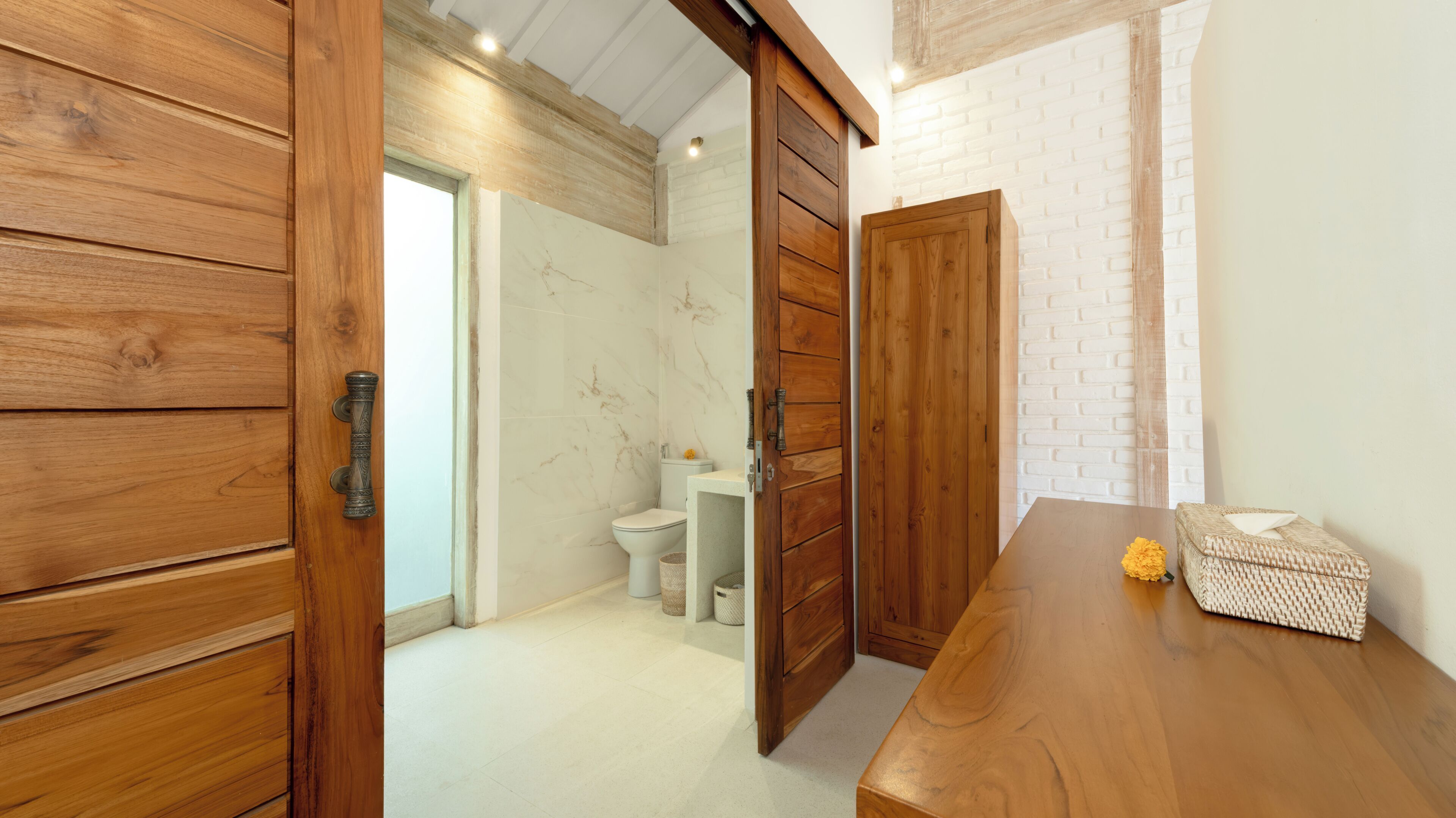 A wooden door leading to a bathroom with a toilet and a marble wall.