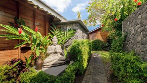 A serene garden with a Buddha statue, lush greenery, and a stone wall. - Villa Taramille by Villa Finder (Kerobokan)