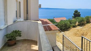 A balcony with a potted plant, a view of the sea, and a building with a red-tiled roof. - Prskalo by Interhome (Omiš)