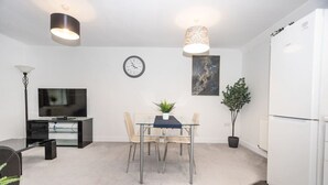 Un salon moderne doté d’un téléviseur à écran plat, d’une table à manger avec des chaises, d’une horloge et de deux lampes suspendues.