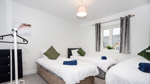 Une chambre avec deux lits, une fenêtre avec des rideaux, un luminaire suspendu et un tableau accroché au mur.