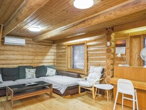 Interior de una cabaña de troncos con sofá, sillas, una mesita y un espacio de escritorio.