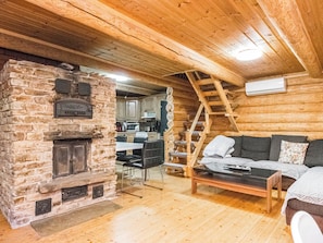 A rustic cabin interior with a stone fireplace, wooden walls, a dining area, and a sofa.