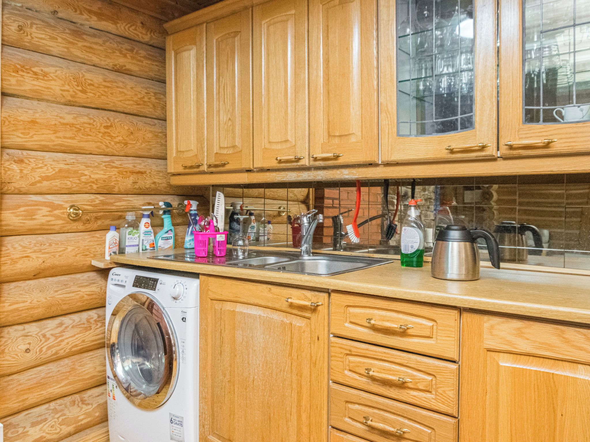 A kitchen with wooden cabinets, a washing machine, and various kitchen utensils.