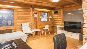 A cozy log cabin interior with a wooden ceiling, a TV, a dining area, and a fireplace.