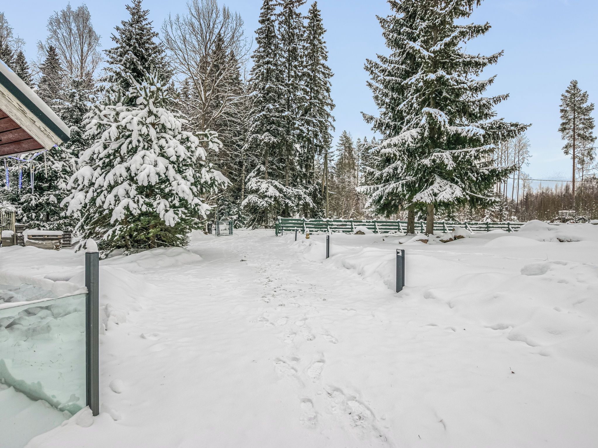 A snow-covered outdoor area with a wooden bench, snow-covered trees, and a clear sky.