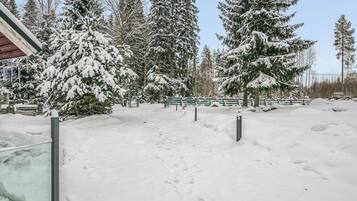 A snow-covered outdoor area with a wooden bench, snow-covered trees, and a clear sky.