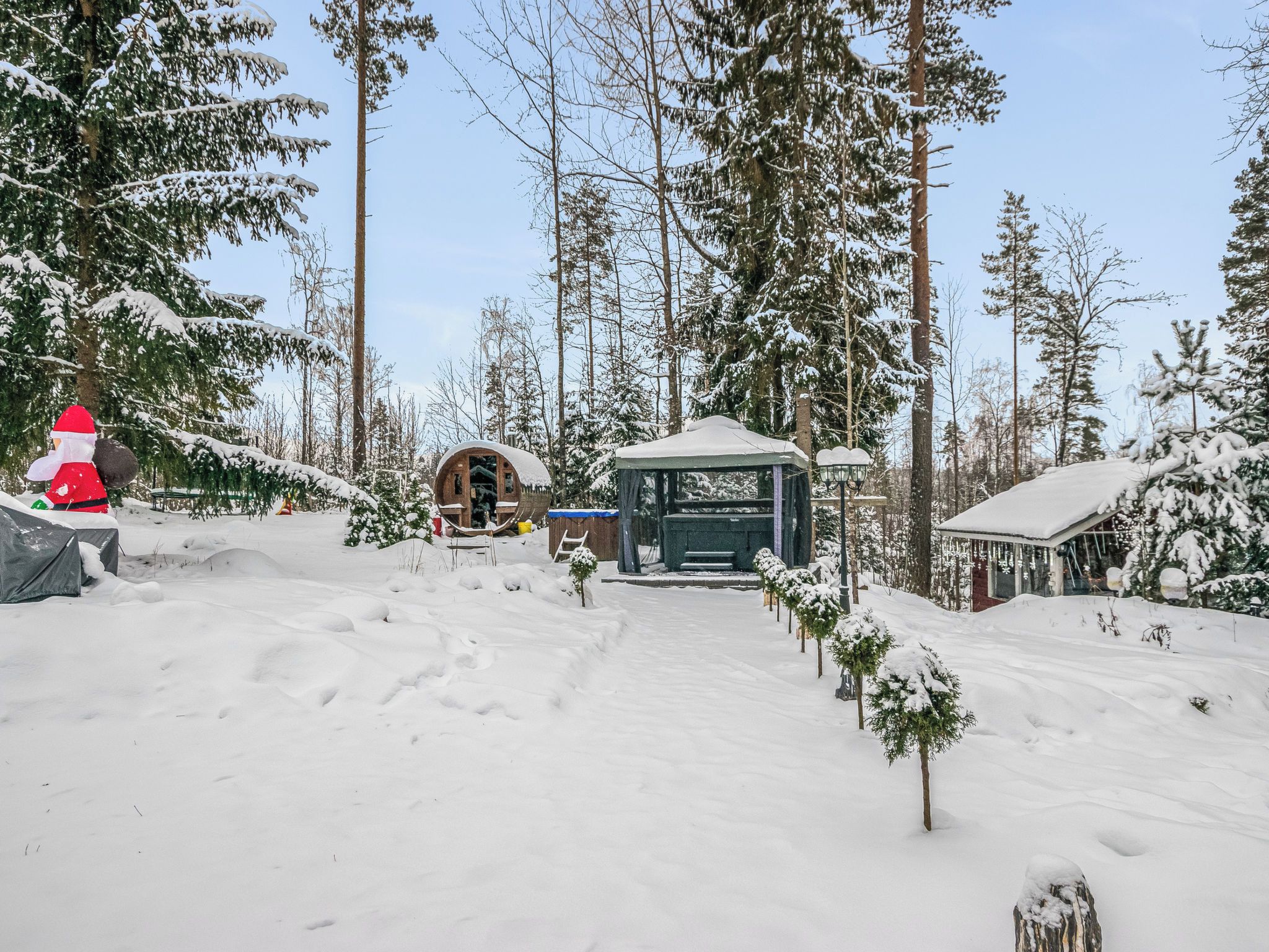 A snow-covered forest with a wooden cabin and a gazebo.