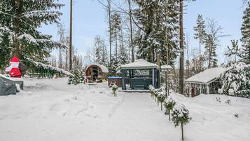 A snow-covered forest with a wooden cabin and a gazebo.