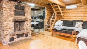 A cozy cabin interior with a stone fireplace, wooden walls, a dining area, and a sofa.