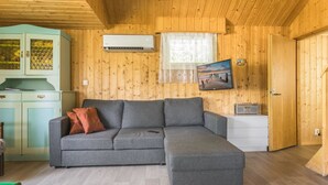 Tunnelmallinen huone, jossa on harmaa kulmasohva, pieni valkoinen kaappi ja seinälle asennettu televisio, josta näkyy kaunis maisema.
