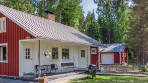Punainen puutalo, jossa on katettu kuisti, grilli ja pieni puutarha-alue.