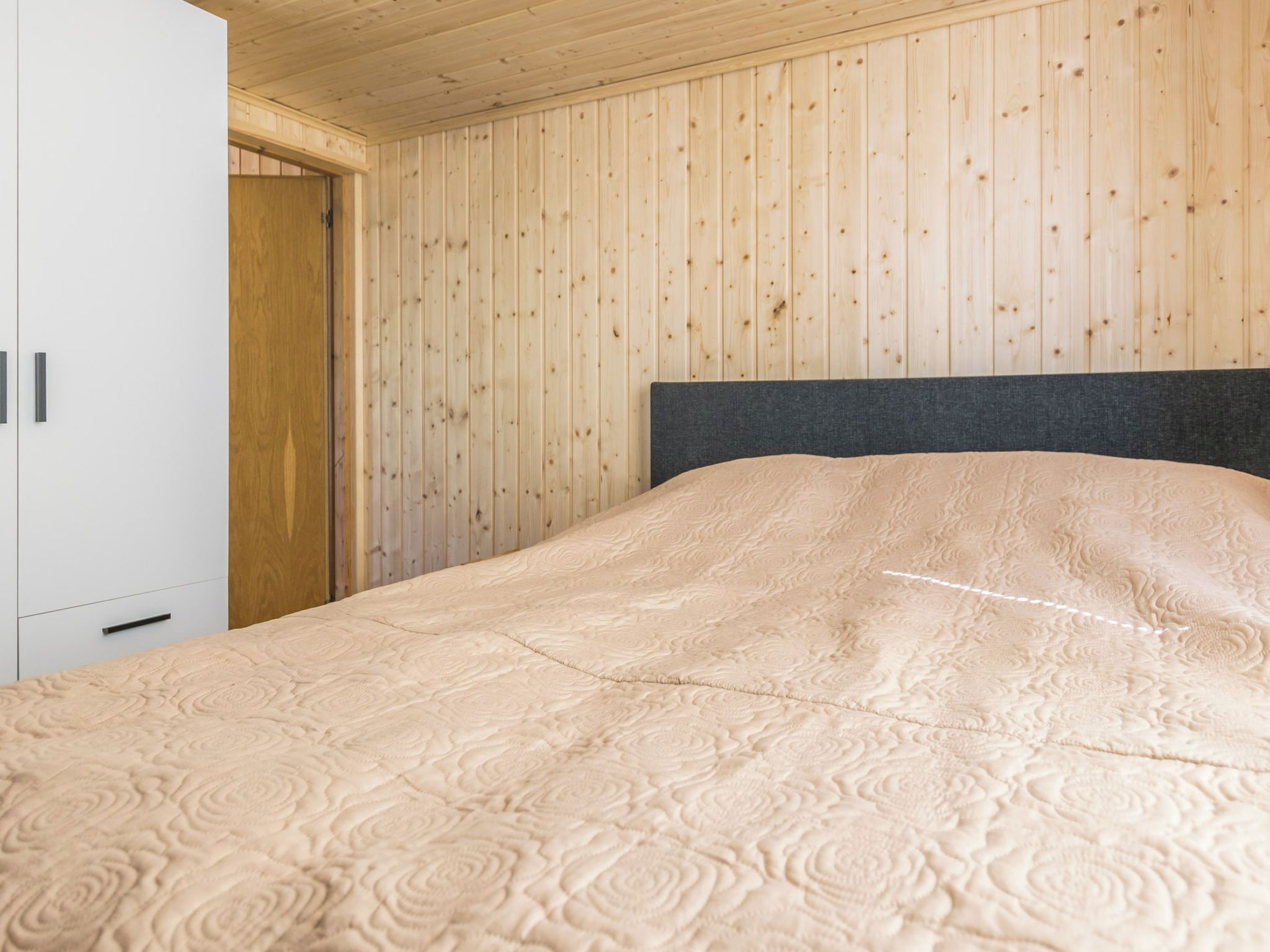 Una camera da letto con un letto, pareti in legno e un armadio bianco.