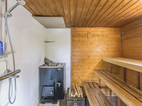 A sauna room with a wooden bench, a sauna heater, and a shower area.